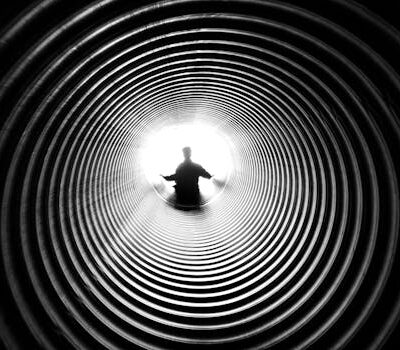 A person silhouetted against light at the end of a spiral tunnel, creating a striking black and white contrast.