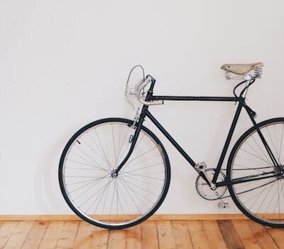 A vintage-style bicycle leaning against a clean white wall with wooden flooring, emphasizing minimalist design.