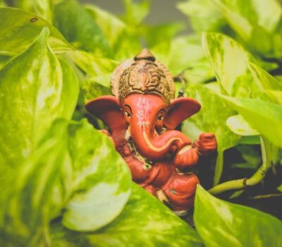A vibrant Ganesha idol surrounded by lush green leaves, representing spirituality and nature.