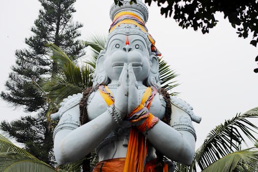 Impressive sculpture of Hanuman with palms, located outdoors among lush greenery.