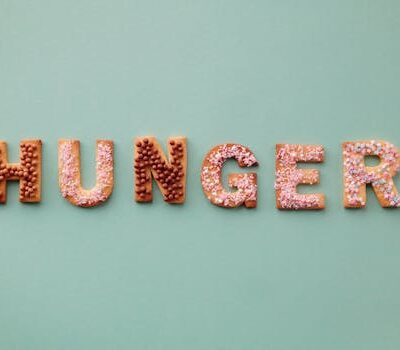 Colorful cookies spelling the word 'Hunger' on a pastel background, topped with sprinkles.