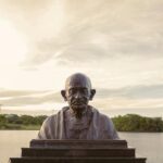 Bronze bust of Mahatma Gandhi with serene lake backdrop in Brasília, Brazil.